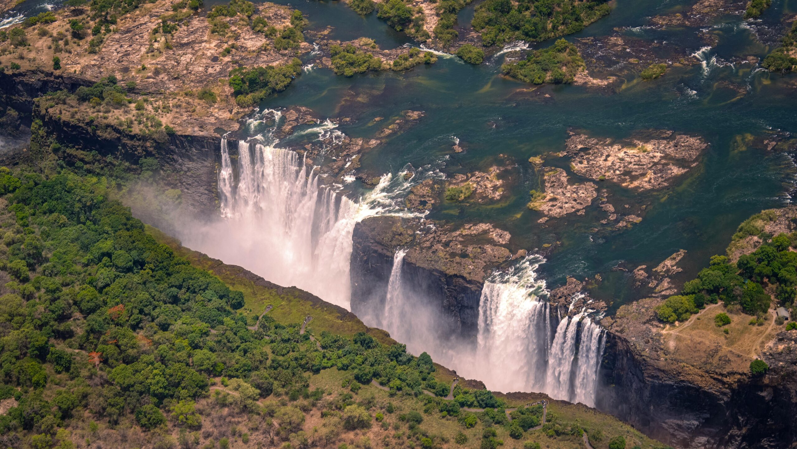 Breathtaking aerial view of Victoria Falls surrounded by lush greenery during summer day.